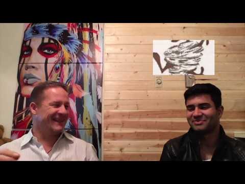 Load video: Young Indian Man talks with Mike Kollin in Video about his Energy Healing Experience doing Timeline therapy with Mike Kollin | Dressed in Black Leather jacket with White T Shirt with colorful 5 foot tall American Indian in back ground