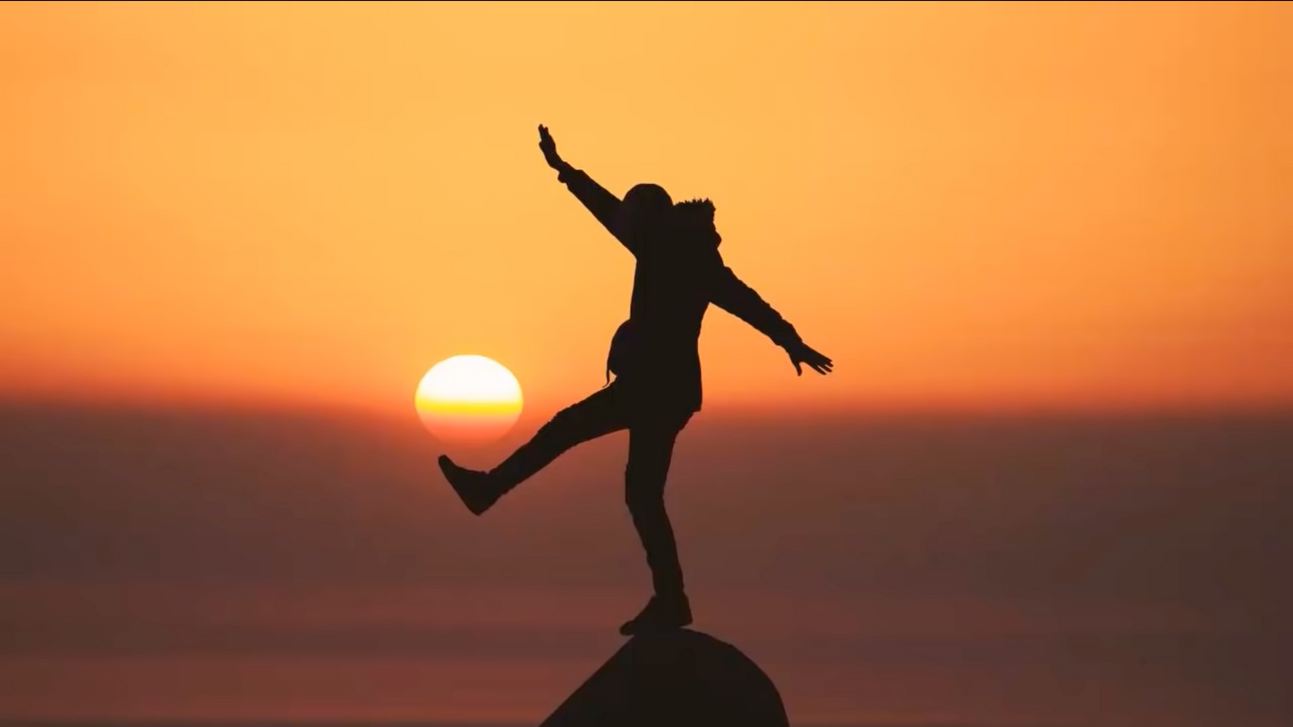 Broken to Bulletproof life coaching - person standing on rock with arms outstretched at sunset representing power and emotional freedom